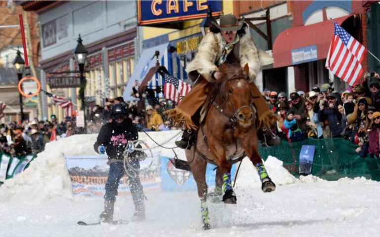 Skijoring action - cowboy on horseback pulling skier through snow-covered main street at a skijoring competition
