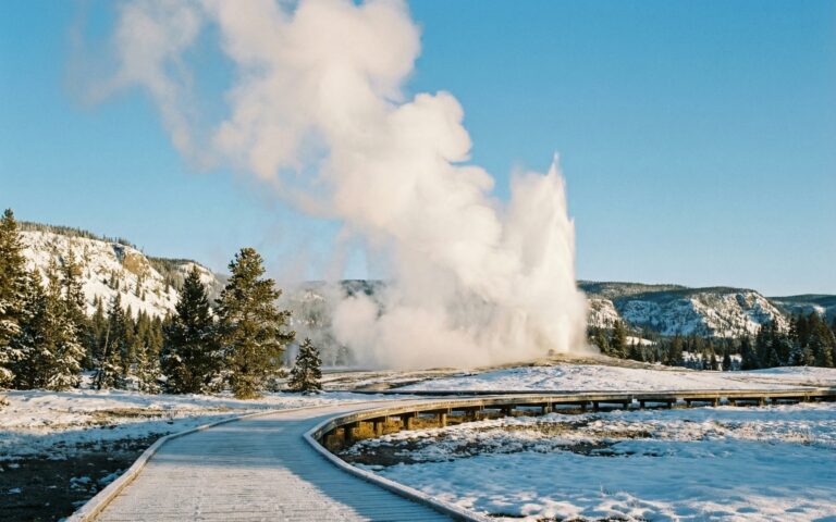 Old Faithful geyser erupting in spring with snow-covered Yellowstone landscape